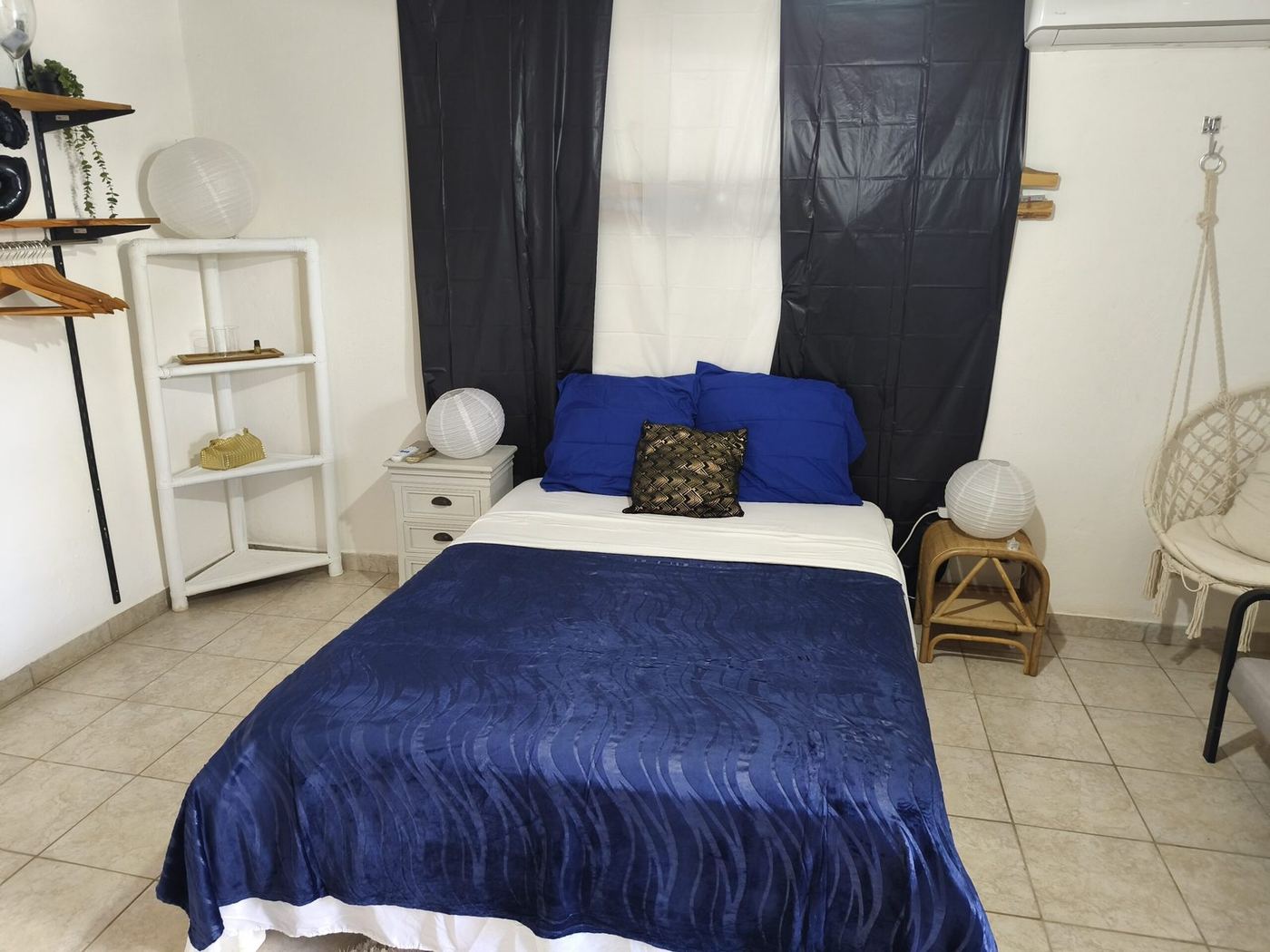 Chambre cosy avec parure bleu marine, fauteuil suspendu et étagères blanches